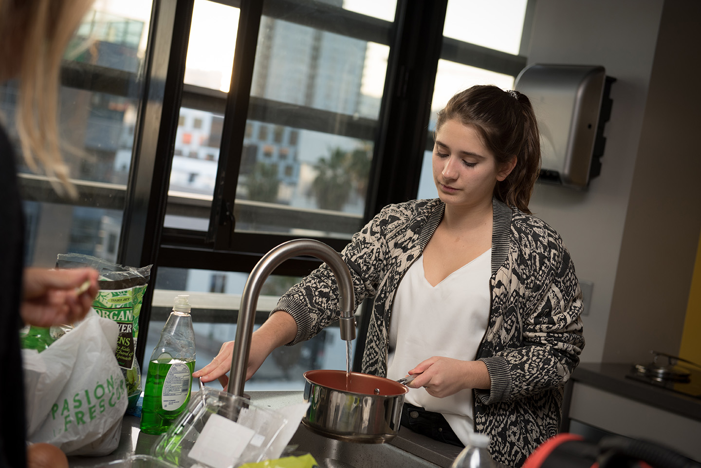 Student in the kitchen space rinsing out pot in the sink